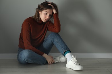 Photo of Sad young woman sitting on floor near grey wall indoors, space for text