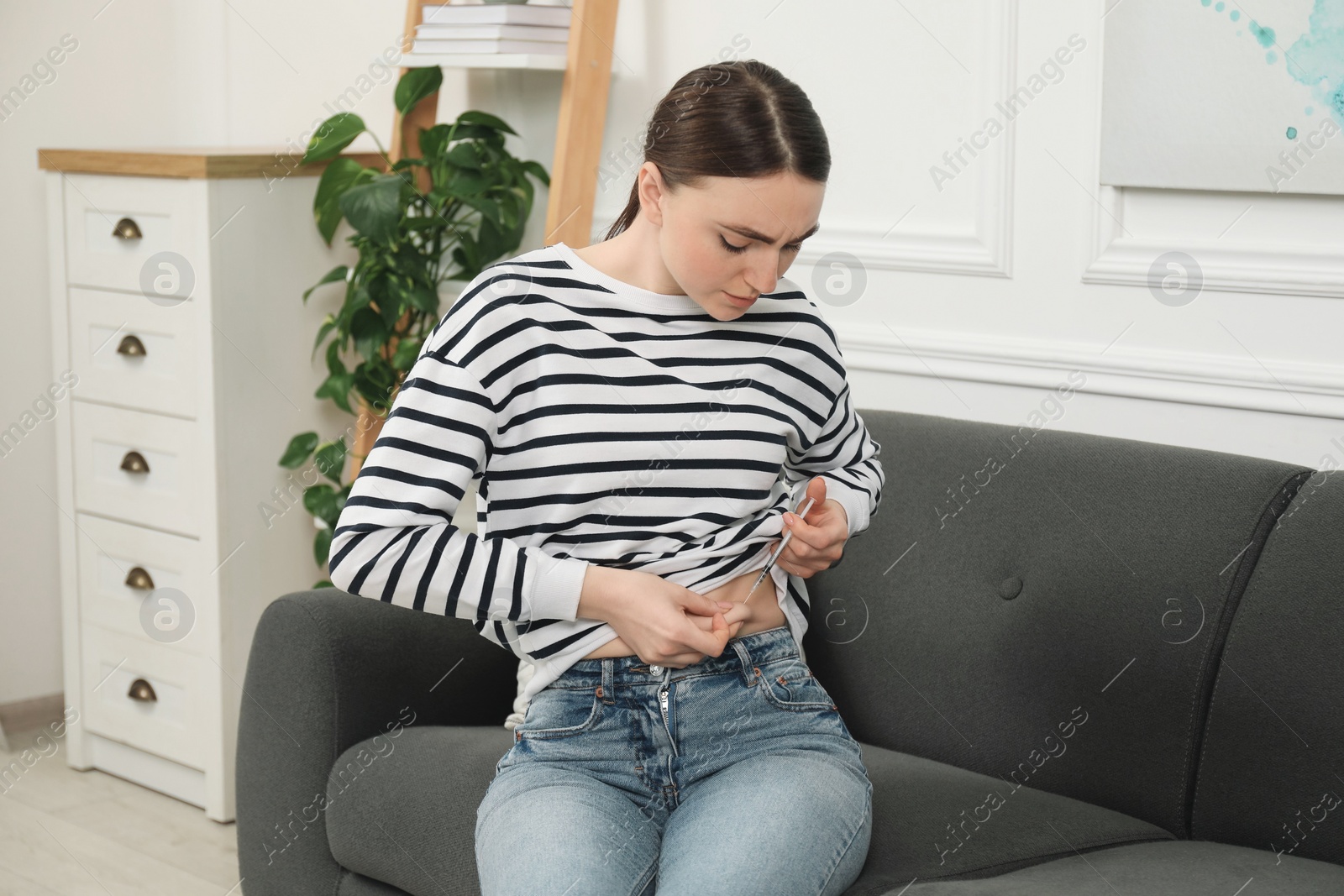 Photo of Diabetes. Woman making insulin injection into her belly on sofa at home