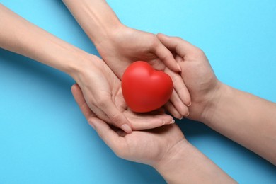 People holding red decorative heart on light blue background, top view. Cardiology concept