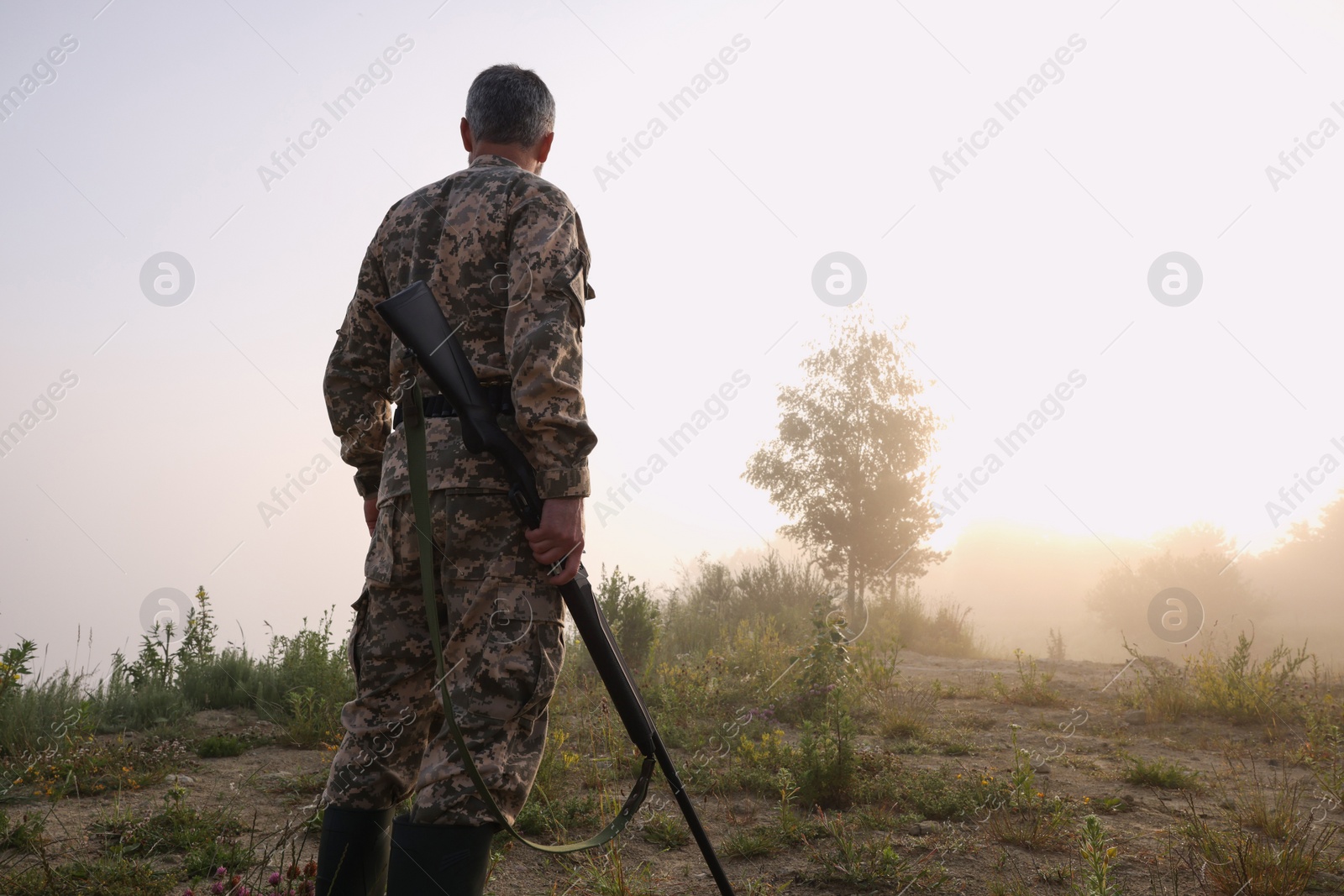 Photo of Man with hunting rifle wearing camouflage outdoors, back view. Space for text