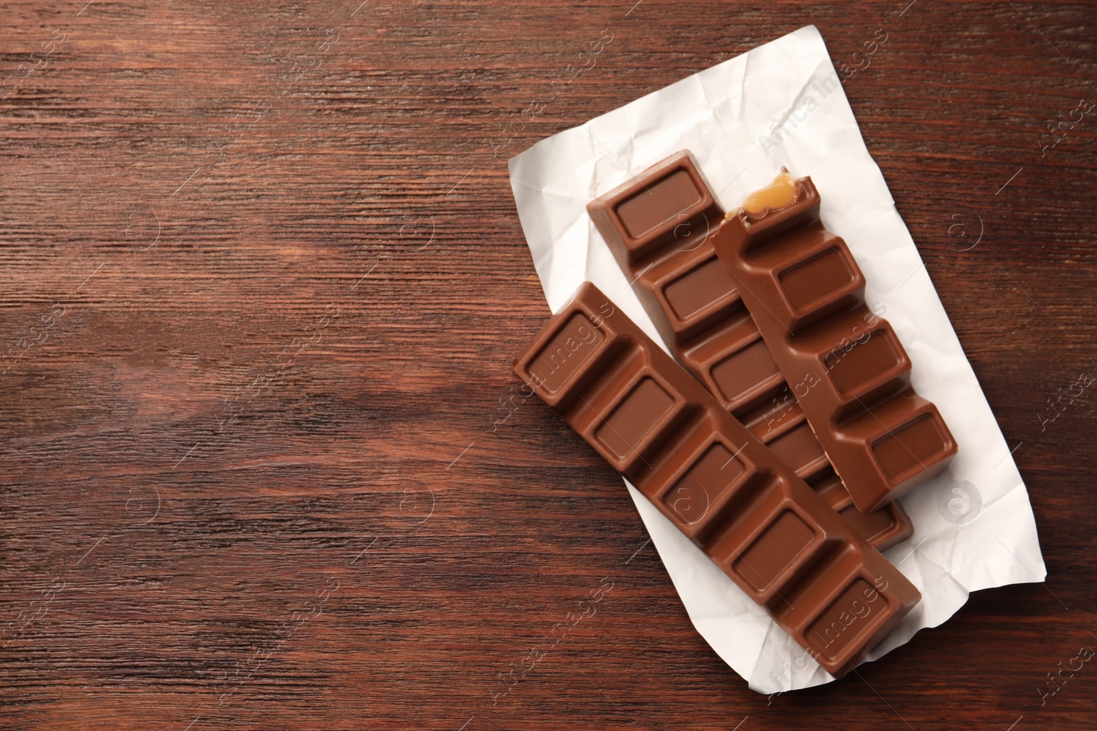 Photo of Tasty chocolate bars on wooden table, top view. Space for text