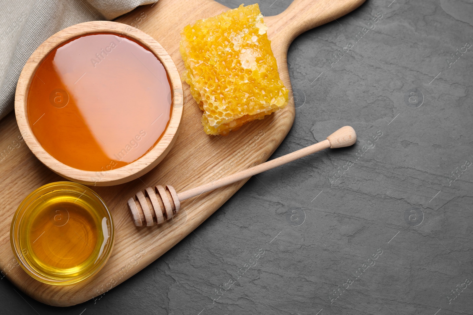 Photo of Sweet honey in bowls, dipper and pieces of honeycomb on grey textured table, flat lay. Space for text