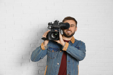 Photo of Operator with professional video camera near white brick wall