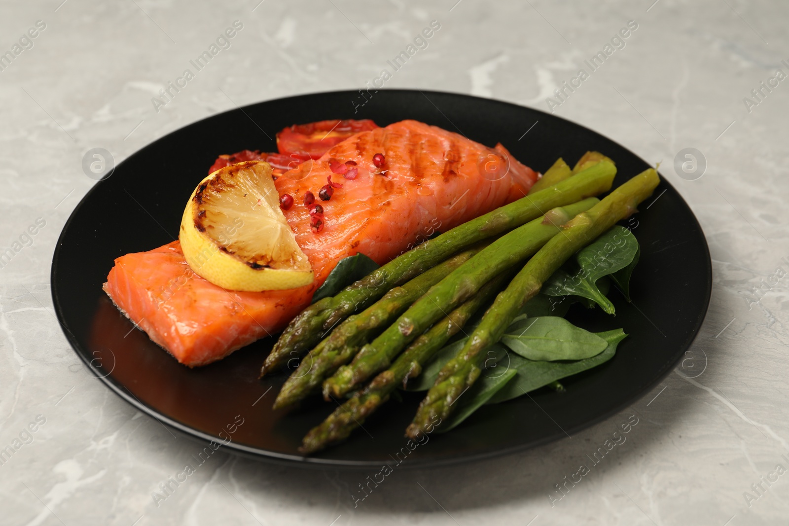 Photo of Tasty grilled salmon with tomatoes, lemon and asparagus on grey table