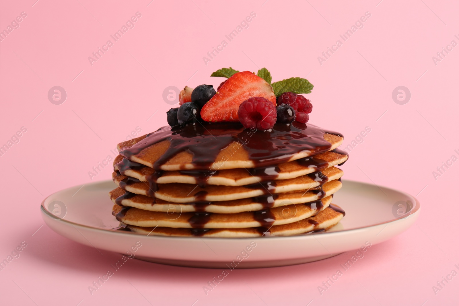 Photo of Stack of tasty pancakes with fresh berries, chocolate sauce and mint on pink background