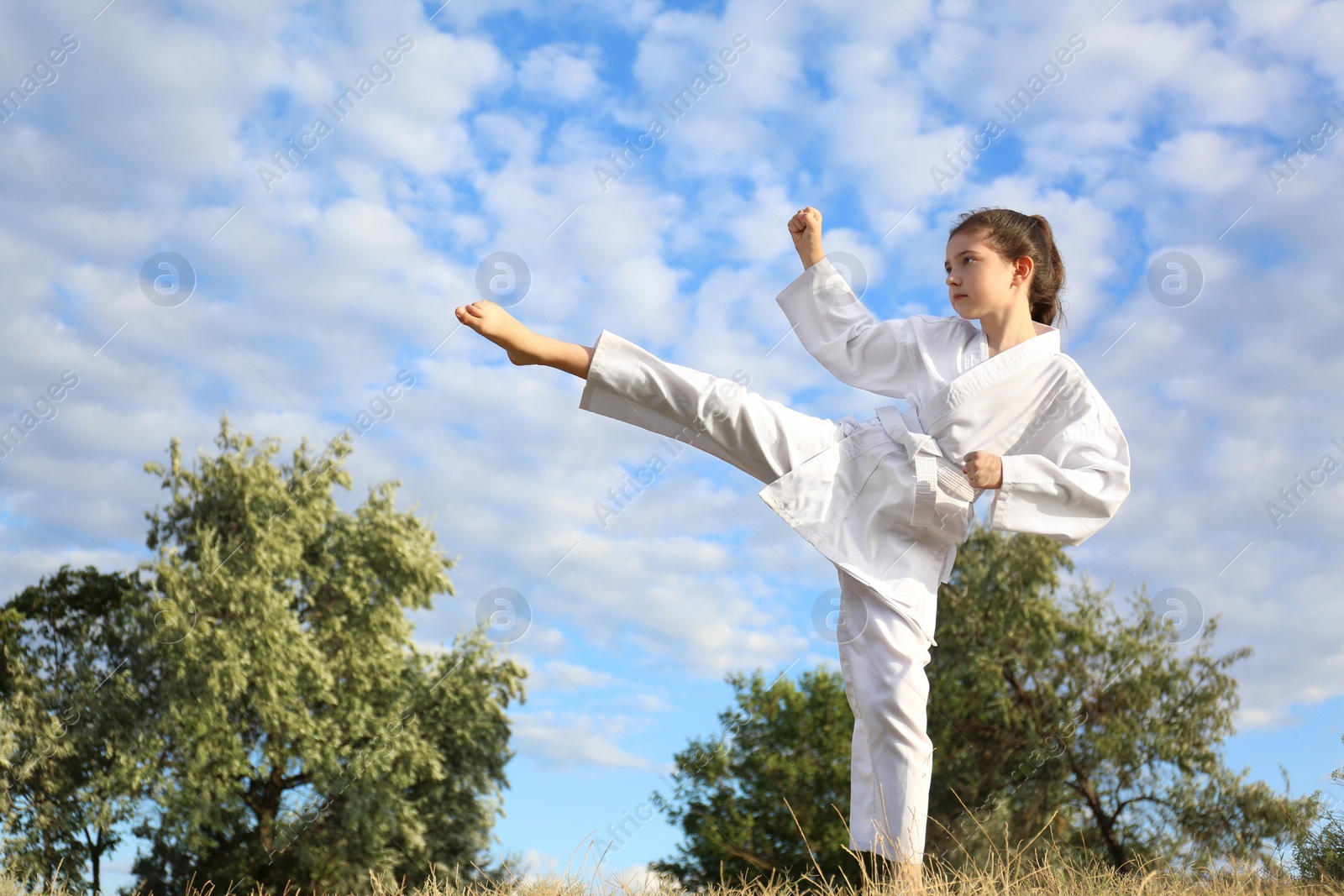 Photo of Cute little girl in kimono training karate outdoors