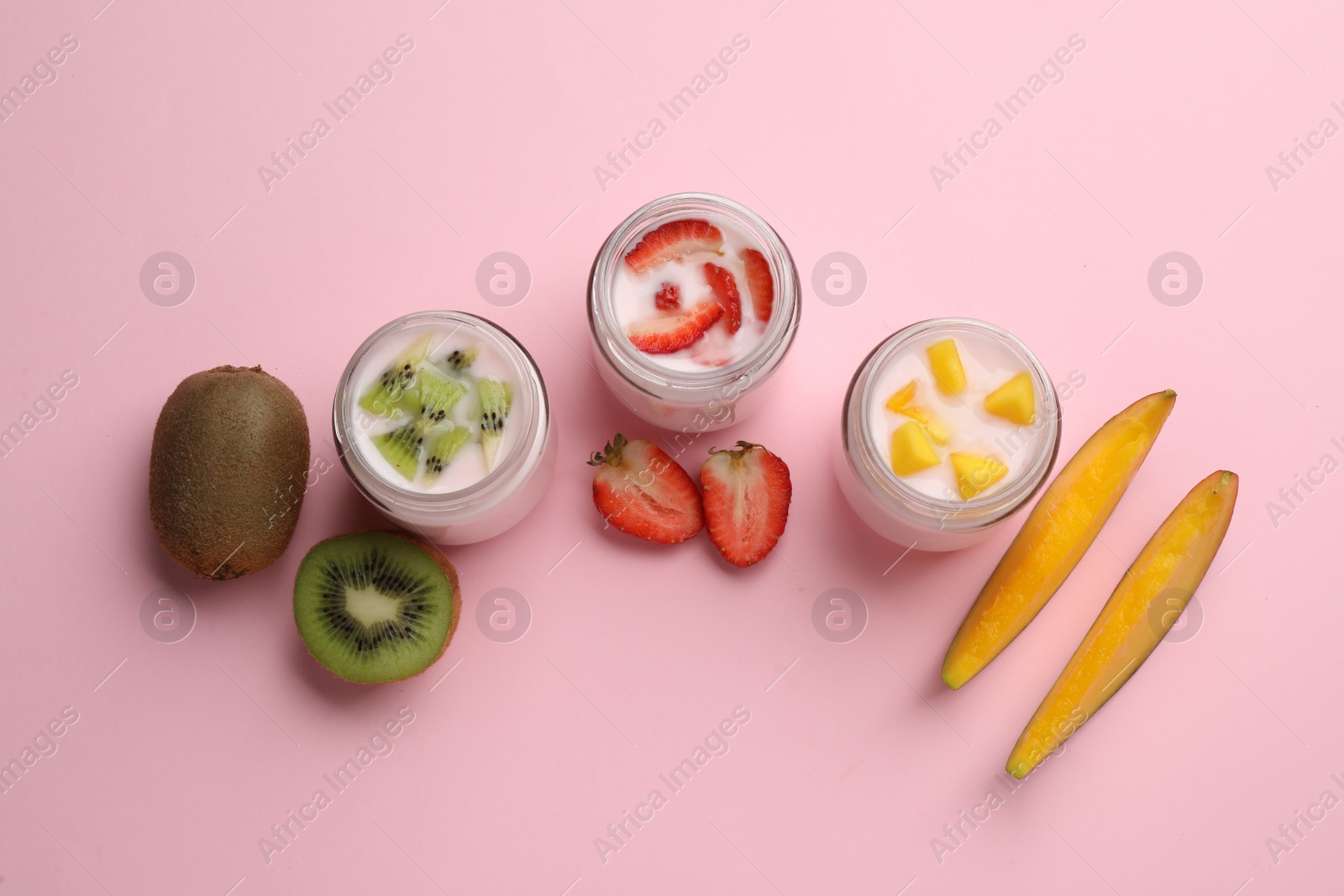 Photo of Tasty yogurt in glass jars and ingredients on pink background, flat lay