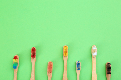 Natural toothbrushes made with bamboo on green background, flat lay. Space for text