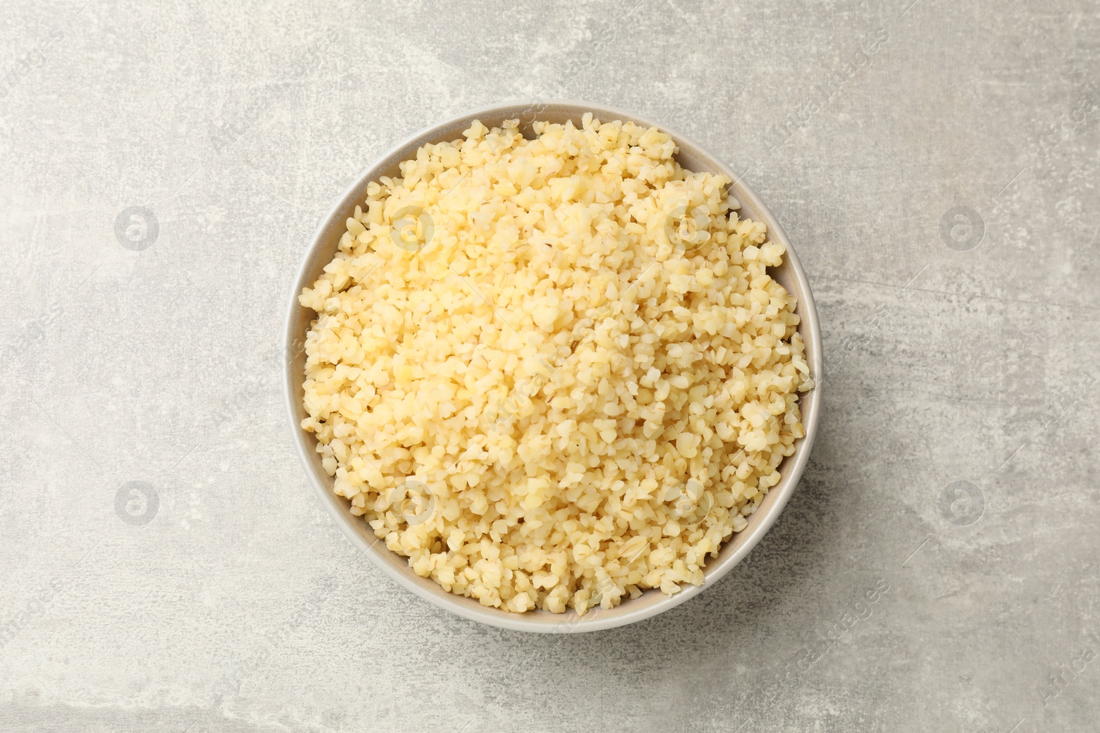 Photo of Delicious bulgur in bowl on gray table, top view