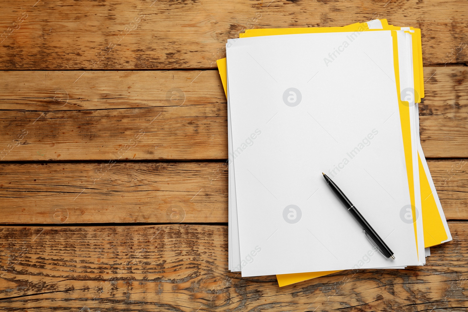 Photo of Yellow files with blank sheets of paper and pen on wooden table, top view. Space for text