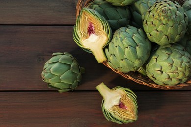 Photo of Wicker basket with fresh raw artichokes on wooden table, flat lay