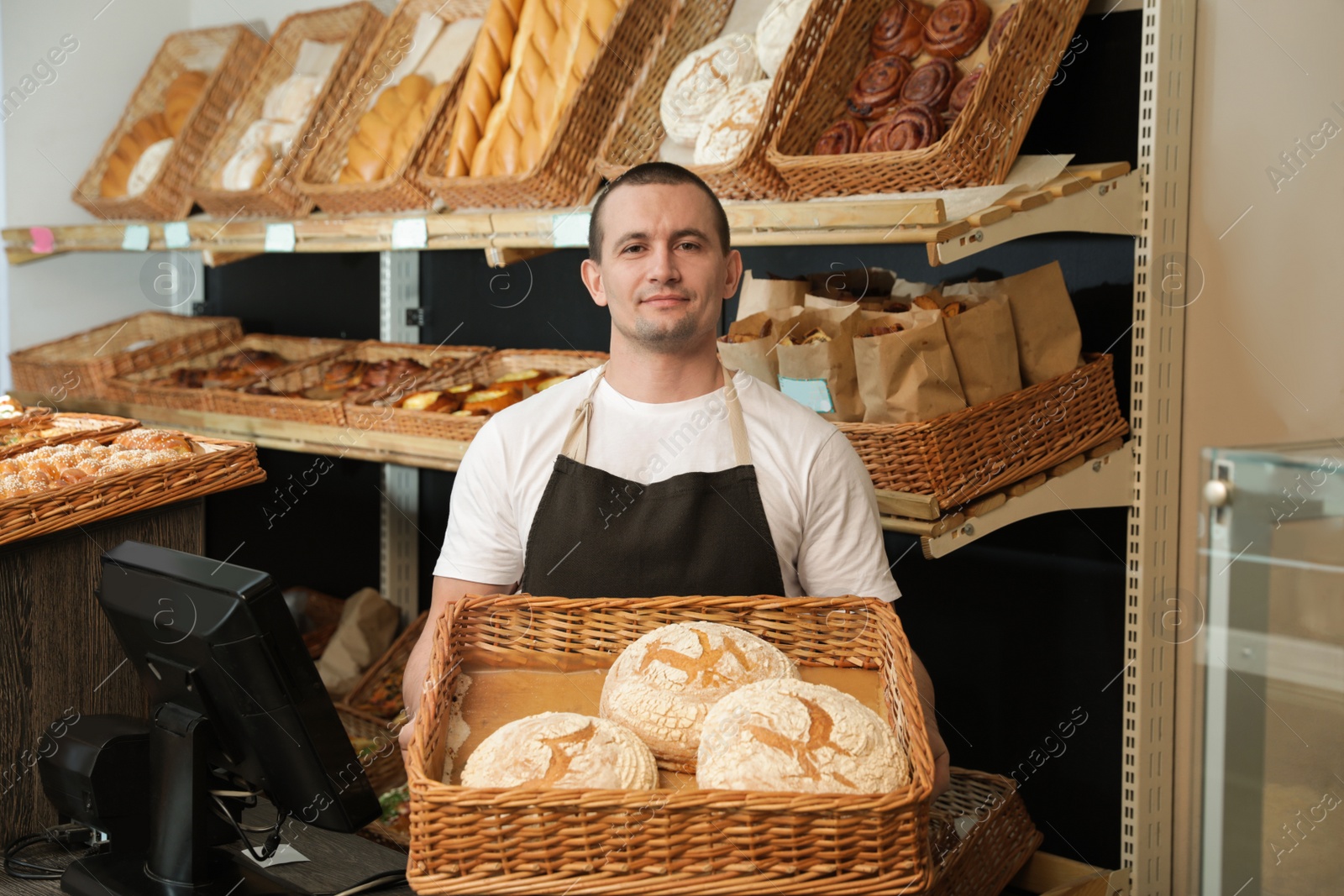 Photo of Portrait of professional baker holding tray with fresh bread near showcase in store