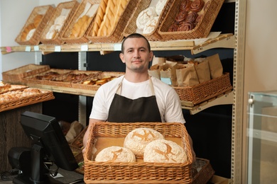 Portrait of professional baker holding tray with fresh bread near showcase in store