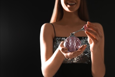 Photo of Young woman with bottle of perfume on black background, closeup. Space for text
