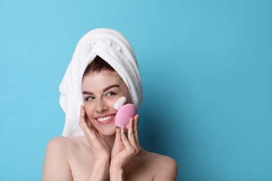 Photo of Young woman washing face with brush and cleansing foam on light blue background. Space for text