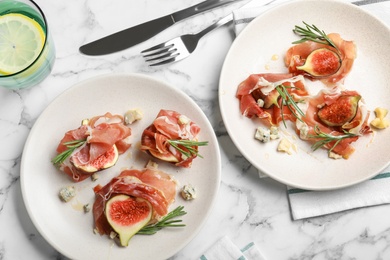 Photo of Delicious ripe figs and prosciutto served on white marble table, flat lay