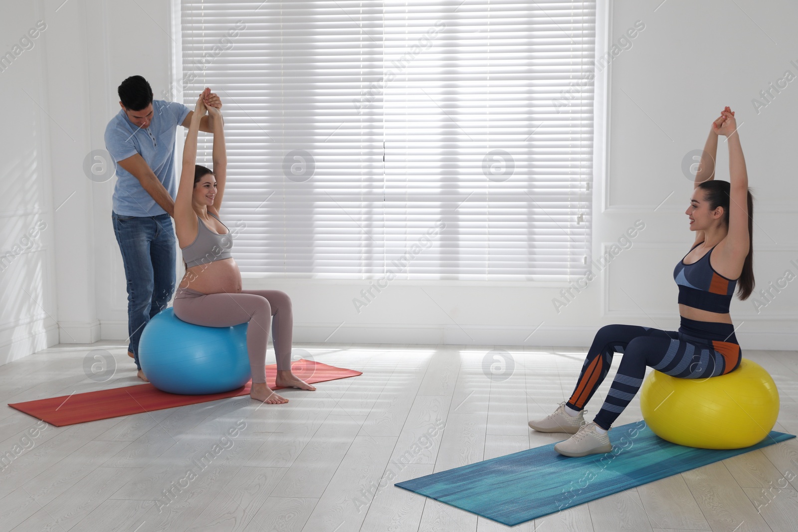 Photo of Pregnant woman and her husband working with trainer in gym. Preparation for child birth