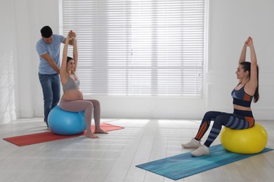 Photo of Pregnant woman and her husband working with trainer in gym. Preparation for child birth