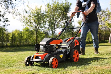 Photo of Man cutting green grass with lawn mower in garden, selective focus