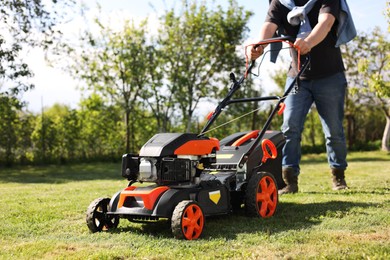 Man cutting green grass with lawn mower in garden, selective focus