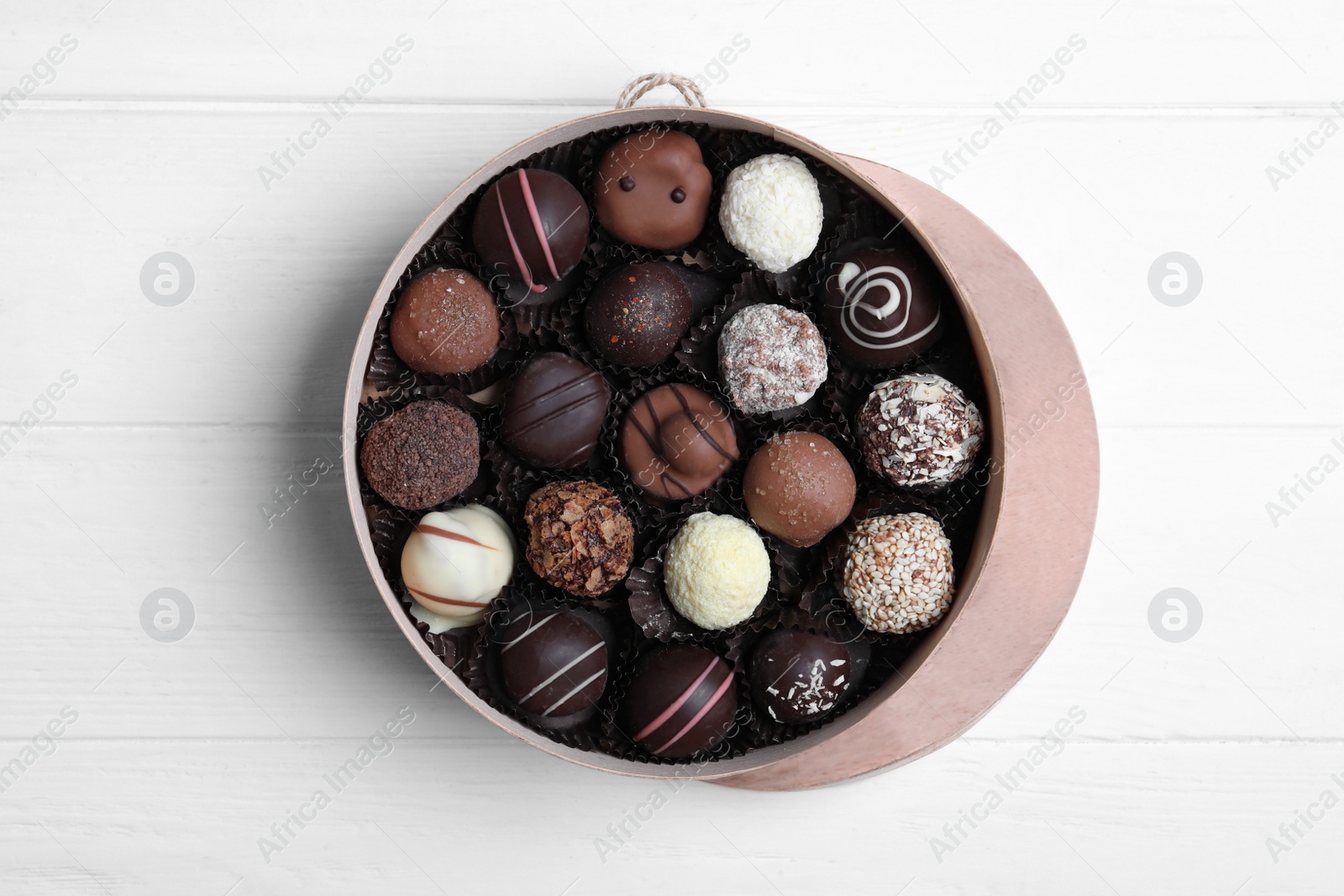 Photo of Box with tasty chocolate candies on white wooden table, flat lay