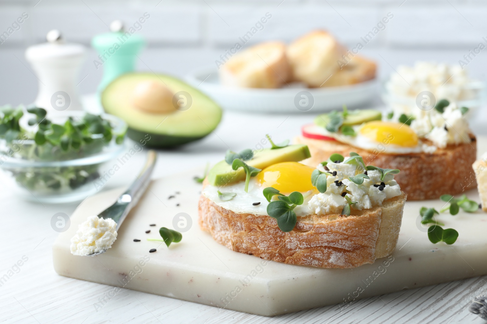 Photo of Delicious sandwiches with egg, cheese, avocado and microgreens on white wooden table