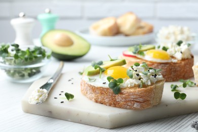 Photo of Delicious sandwiches with egg, cheese, avocado and microgreens on white wooden table