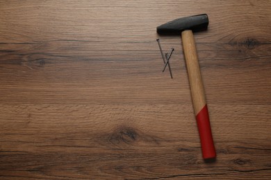 Photo of Hammer and metal nails on wooden table, top view. Space for text