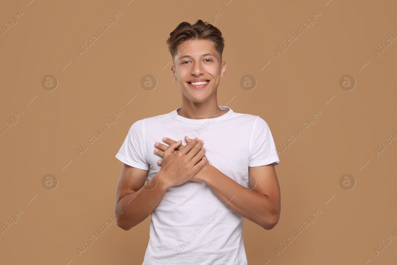 Photo of Thank you gesture. Handsome grateful man with hands on chest against brown background