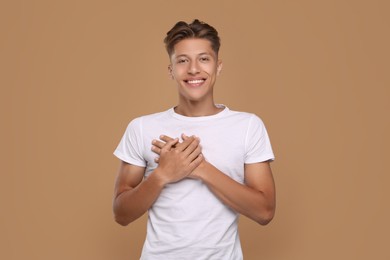 Thank you gesture. Handsome grateful man with hands on chest against brown background
