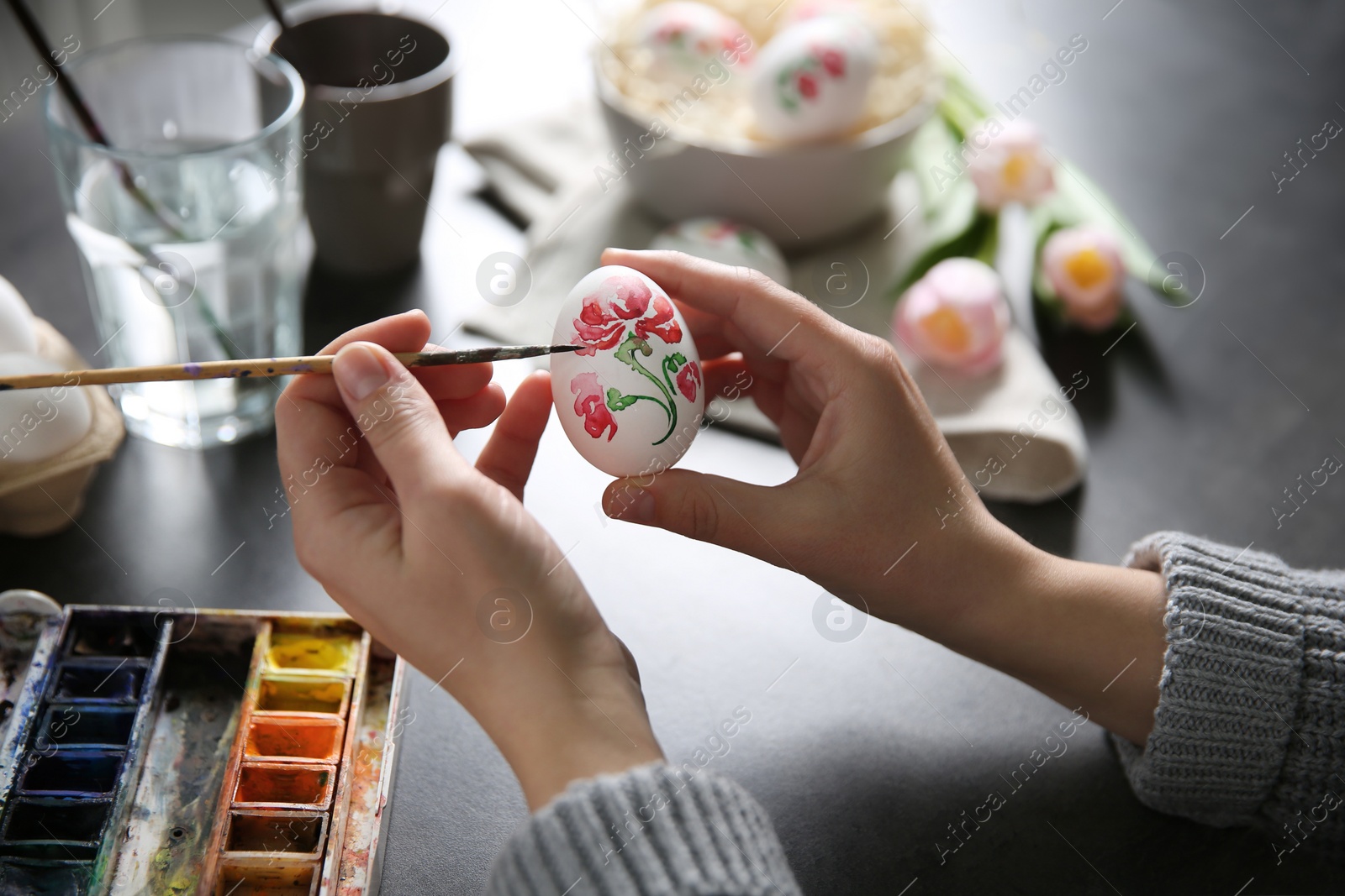 Photo of Woman painting Easter egg at black table, closeup