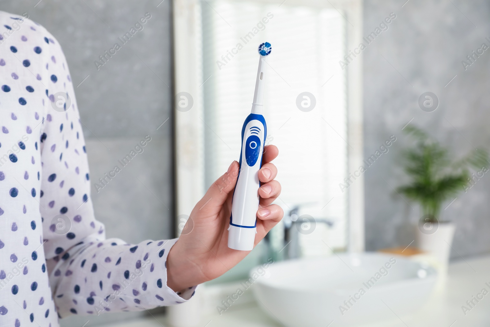 Photo of Woman holding electric toothbrush in bathroom at home, closeup