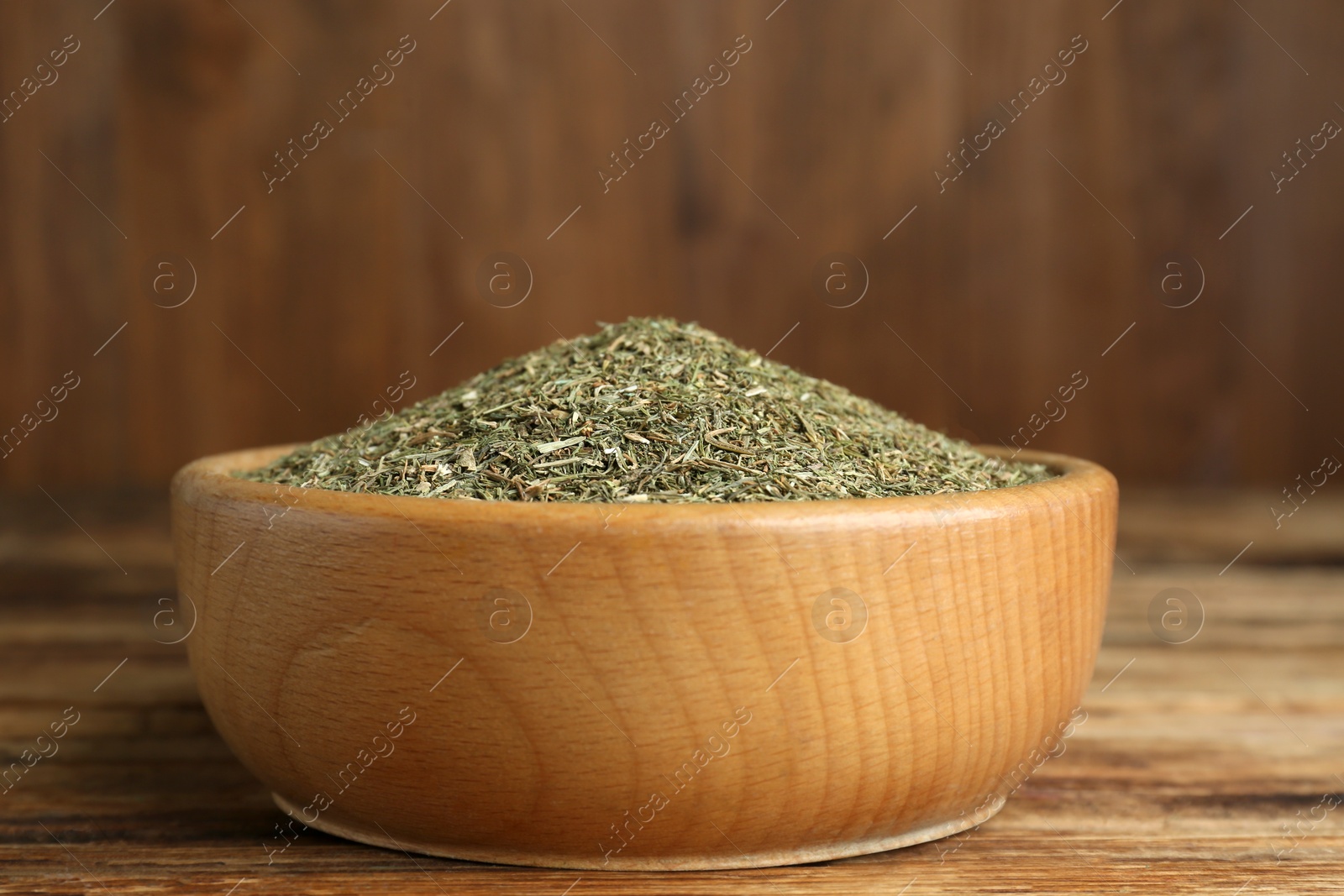 Photo of Bowl of dried dill on wooden table, closeup