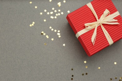 Photo of Red gift box and shiny confetti on grey background, top view. Space for text