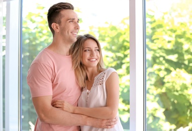 Photo of Happy young couple standing near window at home