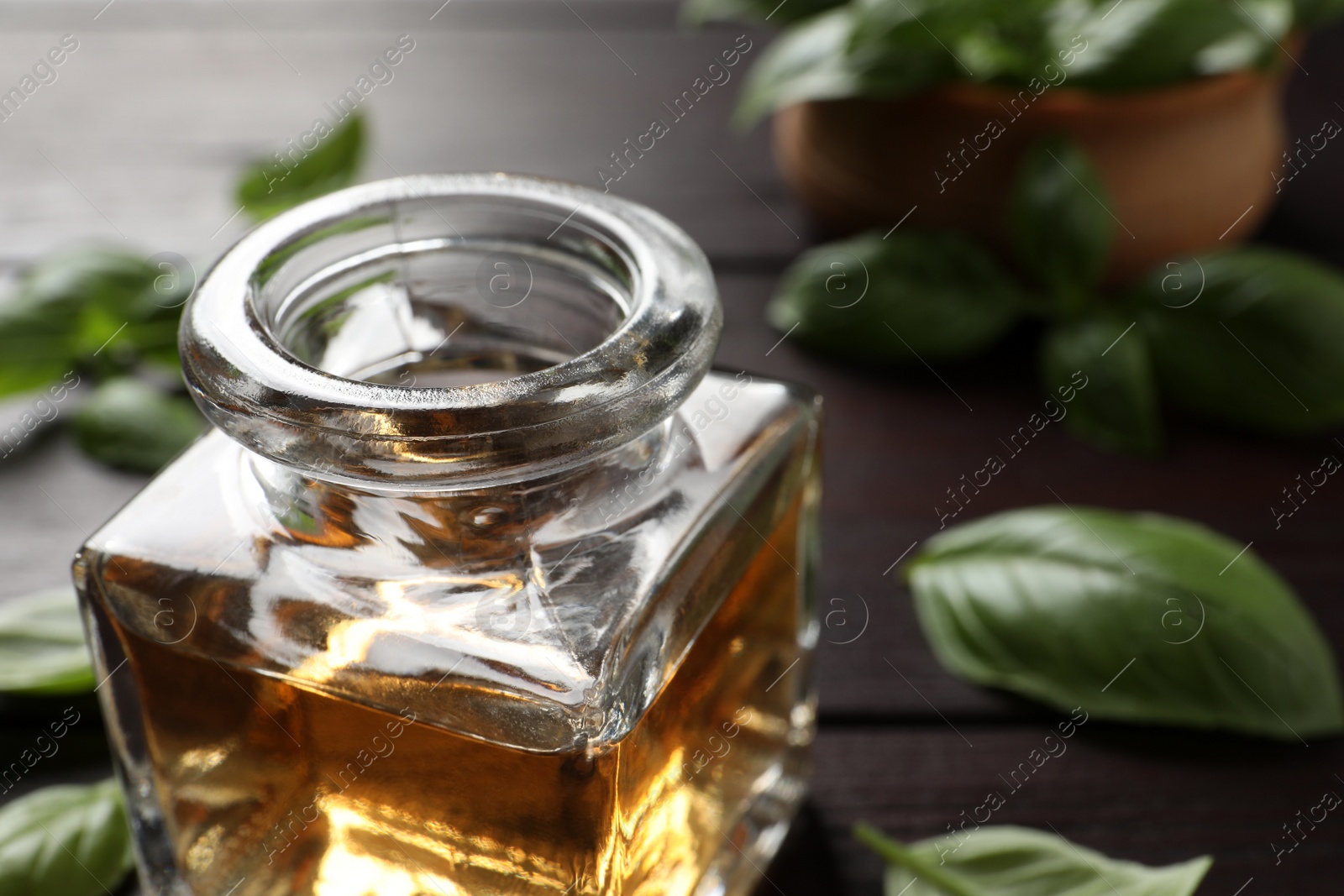 Photo of Glass bottle of basil essential oil and leaves on table, closeup. Space for text