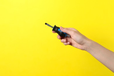 Woman holding small screwdriver on yellow background, closeup. Space for text