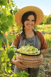 Woman holding fresh green beans in wicker basket outdoors on sunny day