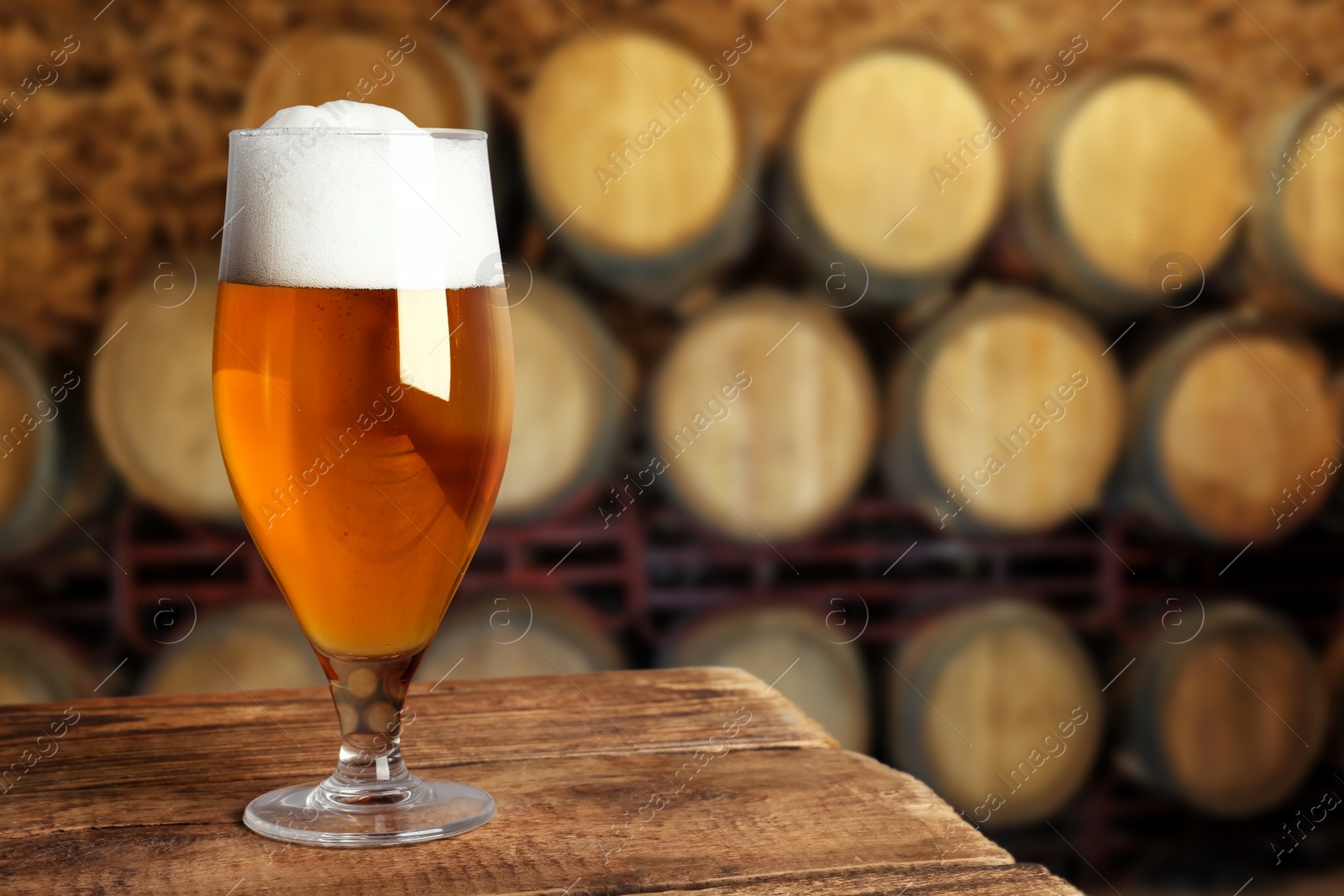 Image of Glass of tasty beer on wooden table in cellar with large barrels, space for text