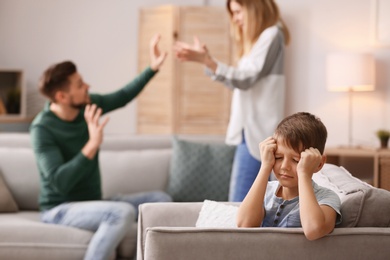 Little unhappy boy sitting in armchair while parents arguing at home