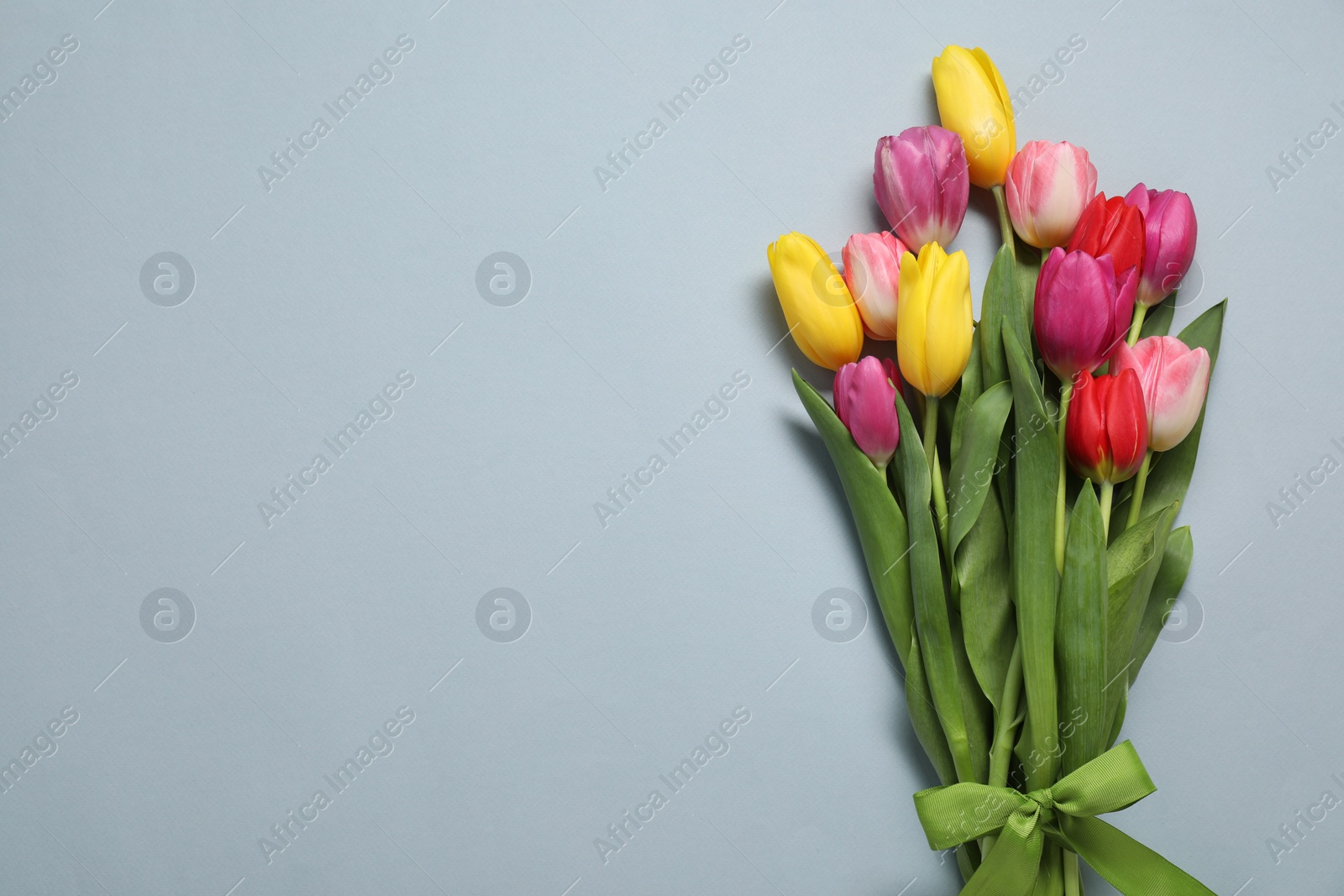 Photo of Beautiful colorful tulip flowers and ribbon on light grey background, flat lay. Space for text