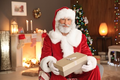 Photo of Santa Claus with gift sitting in armchair at home. Christmas surprise for child