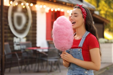 Photo of Stylish young woman eating cotton candy outdoors