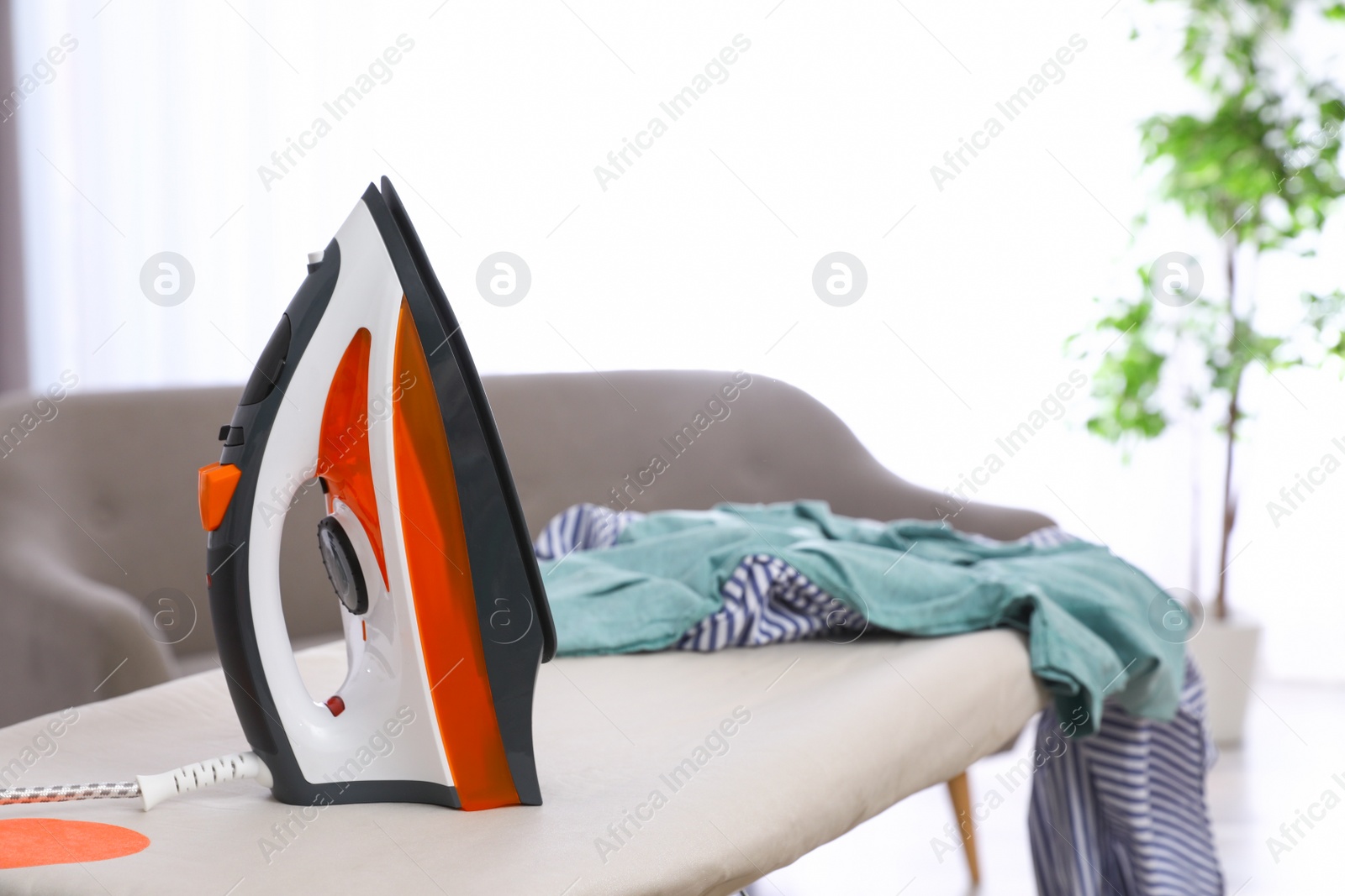 Photo of Modern electric iron and clothes on board indoors. Space for text