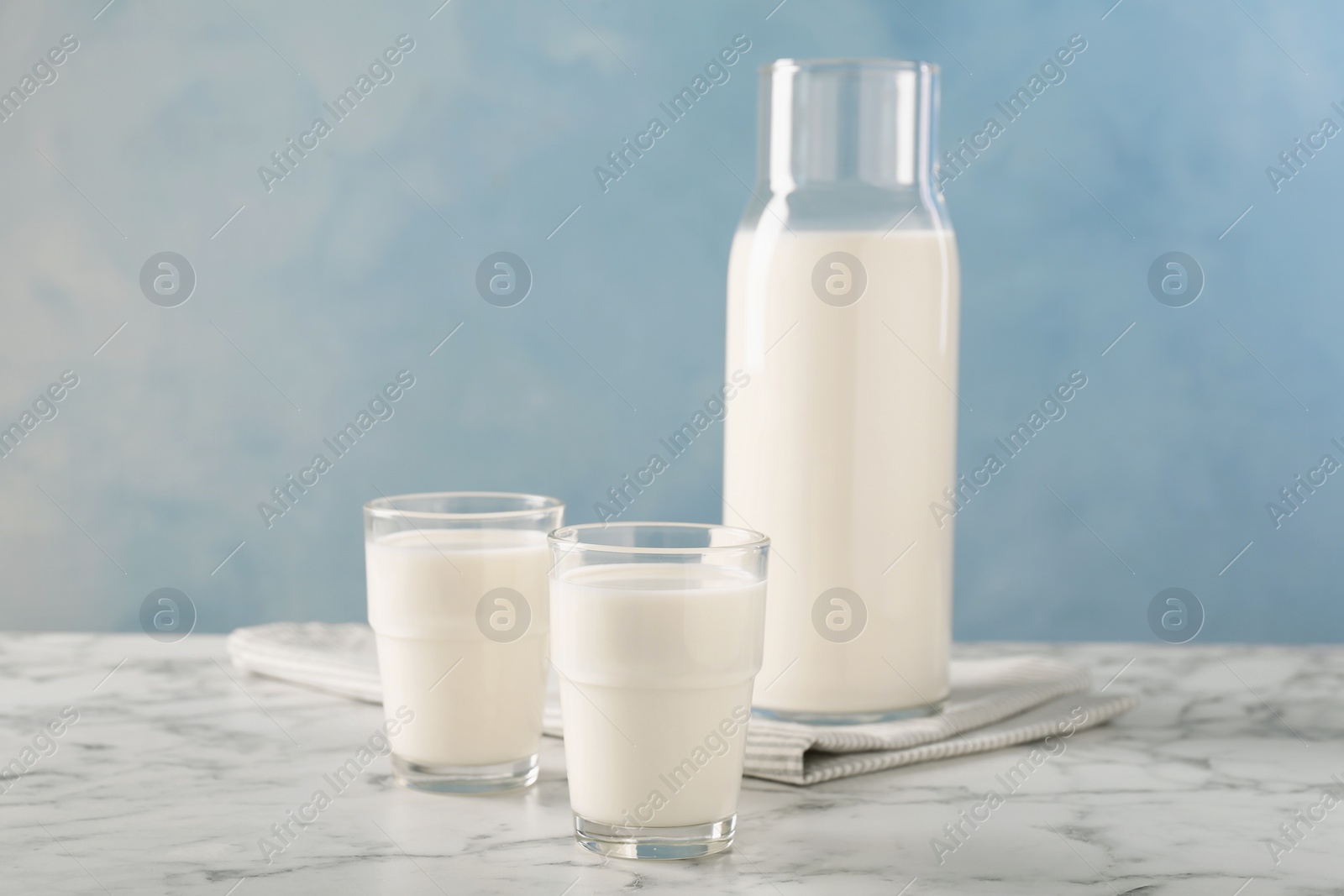 Photo of Carafe and glass of fresh milk on white marble table