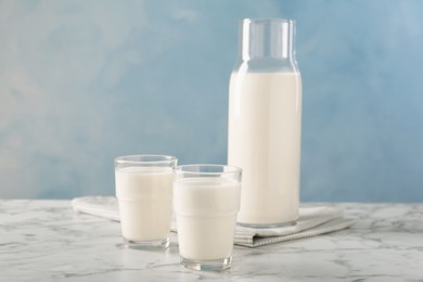 Photo of Carafe and glass of fresh milk on white marble table