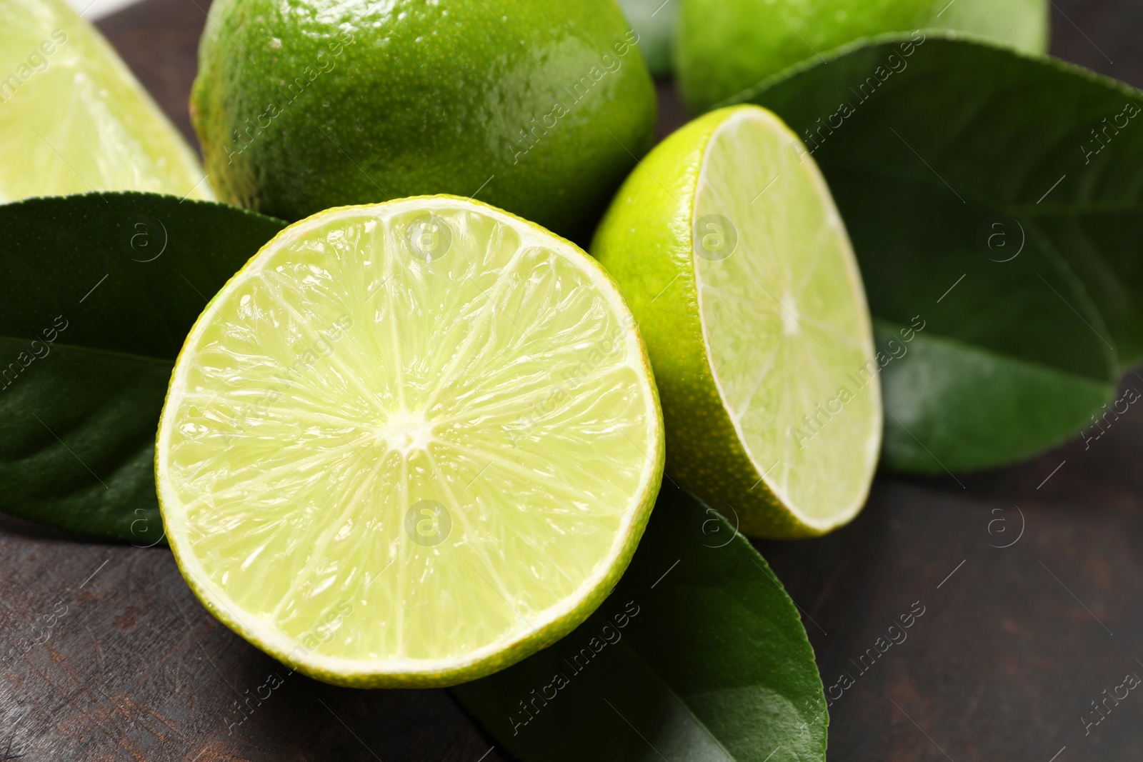 Photo of Fresh ripe limes and green leaves on black board, closeup