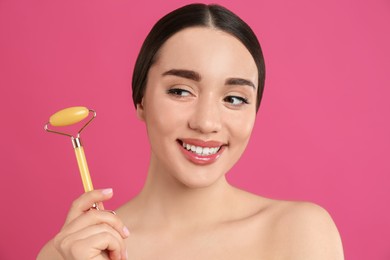 Woman with natural jade face roller on pink background