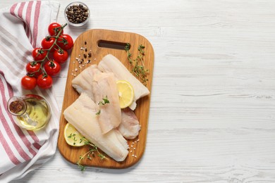 Photo of Pieces of raw cod fish, lemon, tomatoes and oil on white wooden table, top view. Space for text