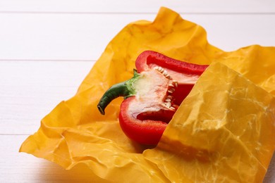 Photo of Half of bell pepper in beeswax food wrap on white wooden table, closeup